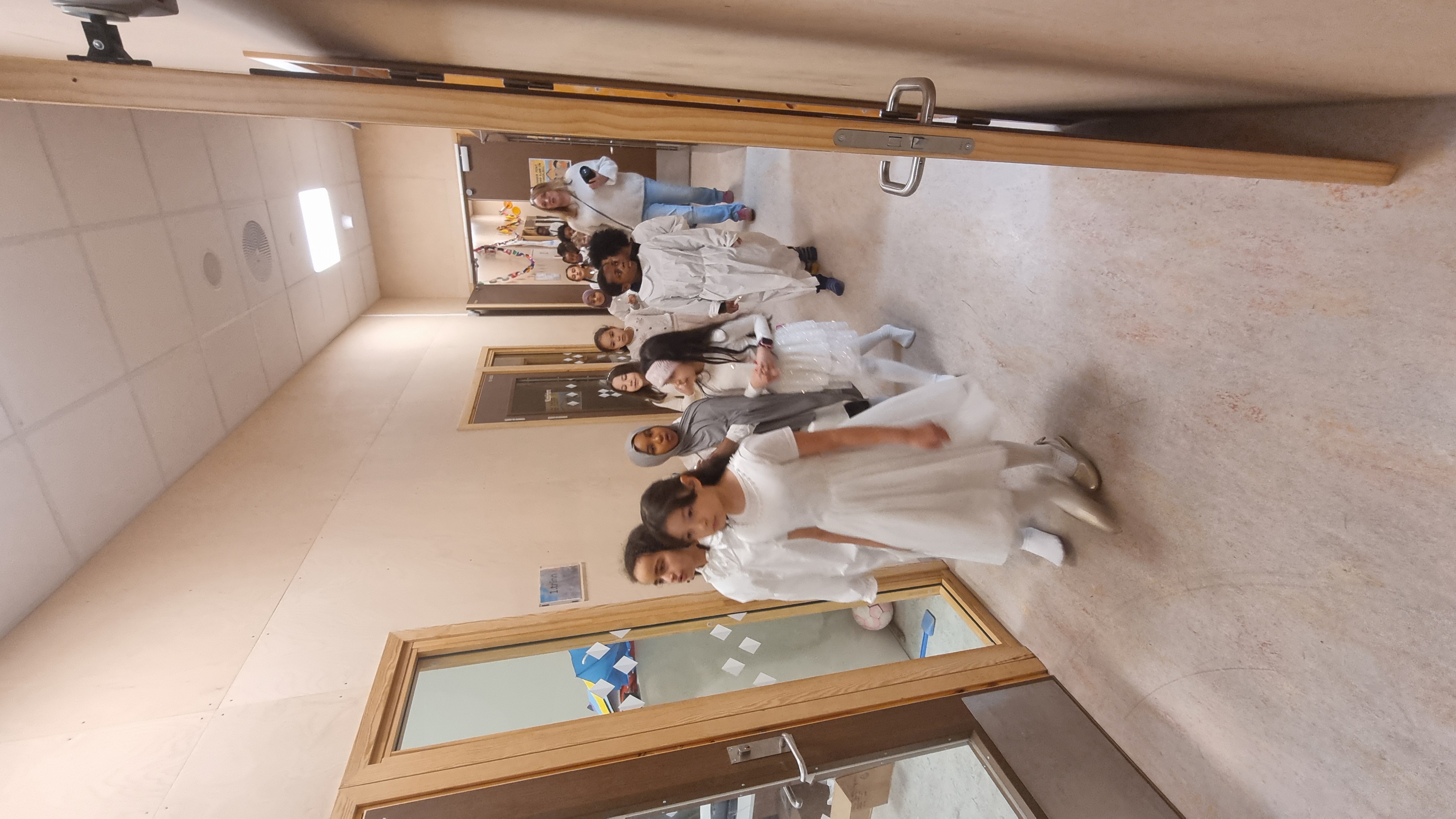 En gruppe mennesker i hvite kjoler går gjennom en korridor